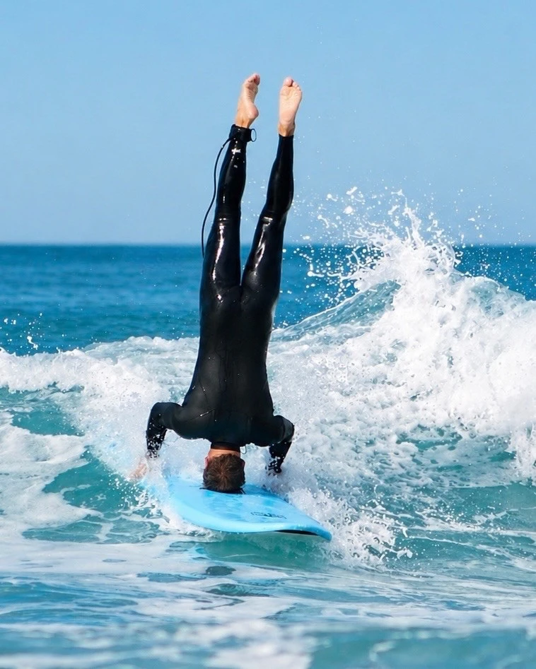Surfeur en combinaison faisant un headstand sur sa planche à Lacanau - The Shack école de surf